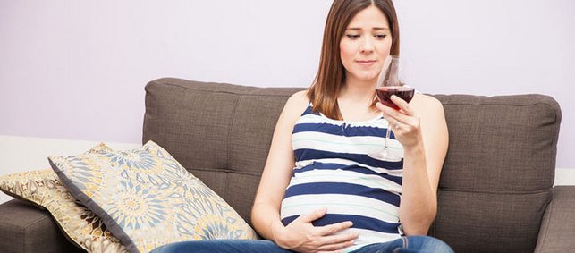 Schwangere sieht zweifelnd auf Weinglas