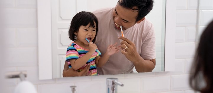 Vater und Kind beim Zähneputzen vor dem Spiegel