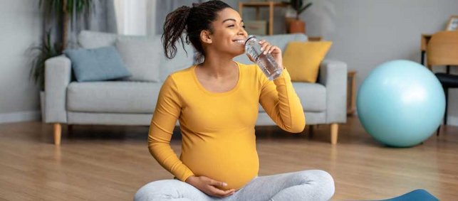 Schwangere auf Yogamatte, Wasser trinkend.