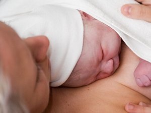 Neugeborenes liegt nach der Geburt mit direktem Hautkontakt auf der Brust der Mutter