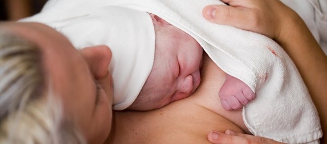 Neugeborenes liegt nach der Geburt mit direktem Hautkontakt auf der Brust der Mutter