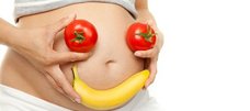 Schwangere hält Tomaten und Banane vorm Bauch als Gesicht