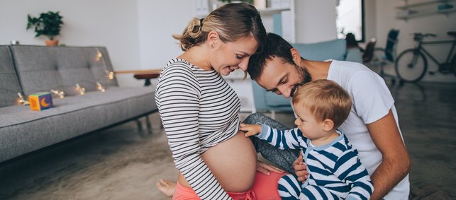 Baby und Papa schauen auf Mamas schwangeren Bauch