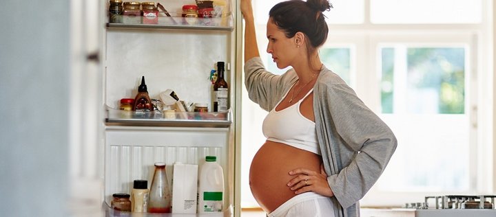 Schwangere Frau schaut nachdenklich in Kühlschrank