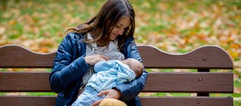 Frau stillt auf einer Parkbank ihr Baby