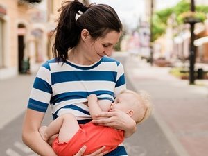 Lächelnde Frau stillt ihr Baby draußen auf dem Gehweg