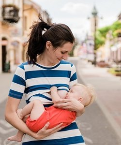 Lächelnde Frau stillt ihr Baby draußen auf dem Gehweg