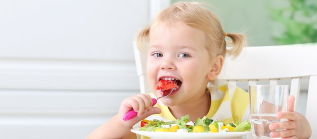 Kleines Mädchen mit Zöpfen isst Salat