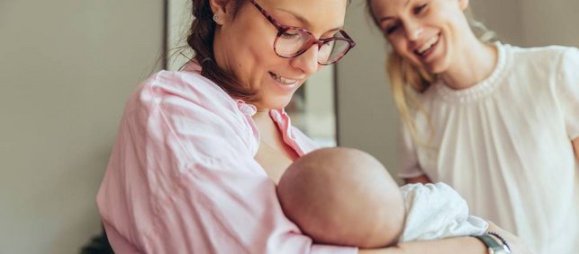 Eine Frau hält ein Baby im Arm, eine andere Frau lächelt dieses an.