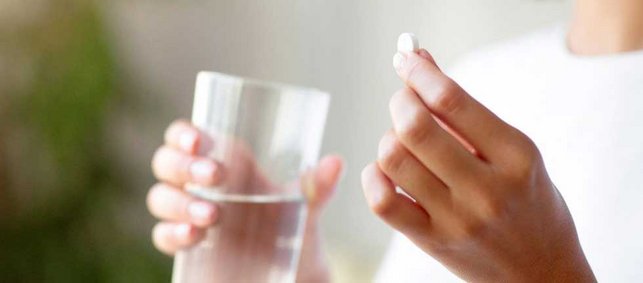 Eine Frau hält eine weiße Tablette in der Hand, in der anderen Hand ein Glas Wasser