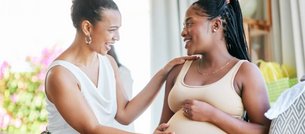 Eine Frau berührt zugewandt den Babybauch einer Schwangeren. 