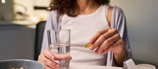 Eine Frau hält eine Kapsel und ein Glas Wasser in der Hand