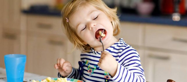 Blondes, etwa dreijähriges Mädchen isst Nudeln ohne Sauce.