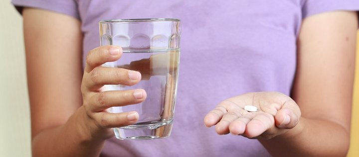 Frau hält eine Tablette und ein Glas Wasser