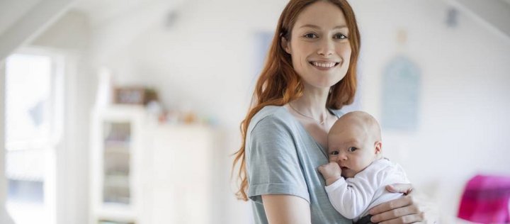 Frau hält stehend ein Baby im Arm und lächelt in die Kamera