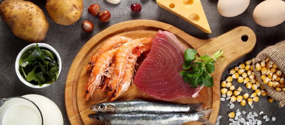 Auf einem schwarzen Tisch liegen verschiedene jodreiche Lebensmittel wie Fisch, Eier und Milchprodukte