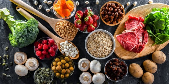 Auf einem Tisch liegt eine Auswahl an eisenreichen Lebensmitteln wie Fleisch, Brokkoli und Bohnen