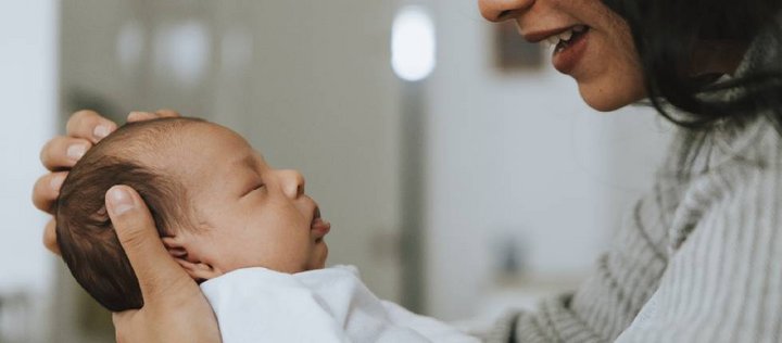 Eine Frau und ein baby sind im profil zu sehen, sie sind einander zugewandt. Die Frau hält das Baby in den Armen. 