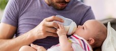 Mann hält Baby im Arm und füttert es mit dem Fläschchen