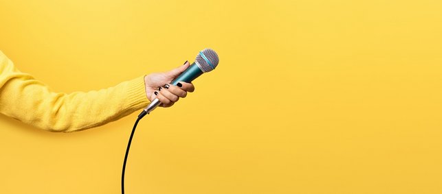 Hand hält Mikrofon, auf gelbem Hintergrund