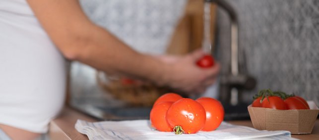 Schwangere wäscht eine Tomate am Waschbecken