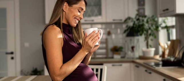 Eine lachende Frau steht in der Küche mit einer Tasse Kaffee in der Hand