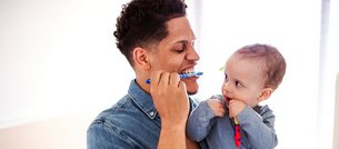 Vater übt mit seinem Baby sanft Zähneputzen
