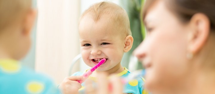 Lächelndes Baby mit Zahnbürste mit Mutter