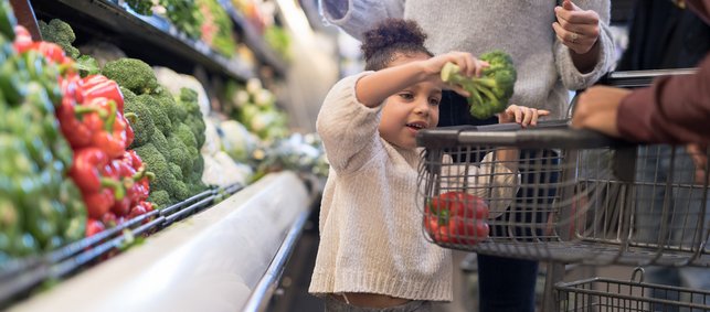 kleines Mädchen legt Gemüse in Einkaufswagen