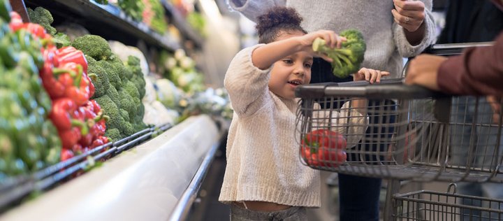 Mädchen in Supermarkt legt Gemüse in Einkaufswagen.