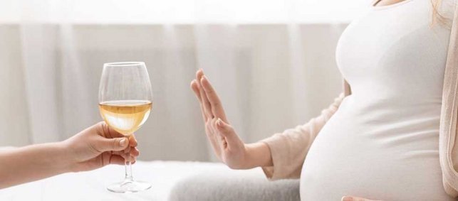 Schwangere macht abweisende Geste mit der Hand gegen ein Glas Wein.