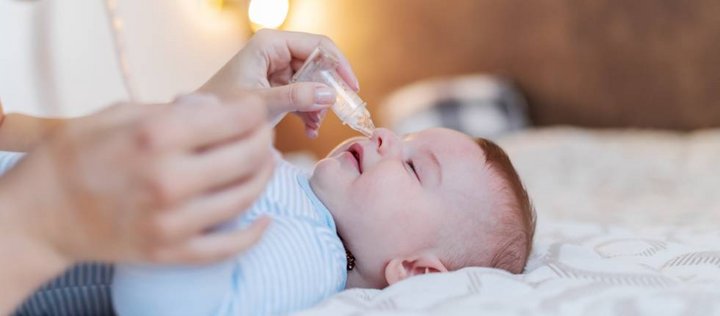 Ein Baby bekommt von einer erwachsenen Person die Nase mit einem Nasensauger gesäubert. 