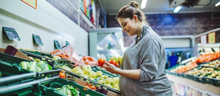 Schwangere Frau am Gemüseregal hält Tomaten in der Hand