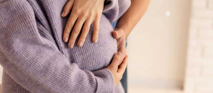 Ein Bauch einer schwangeren Frau, deren Babybauch von drei Händen berührt wird