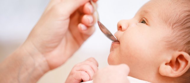 liegendes Baby bekommt etwas mit dem Löffel in den Mund