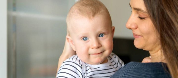 Ein etwa einjähriges Baby schaut den Betrachter an. Es befindet sich auf dem Arm einer Frau. 