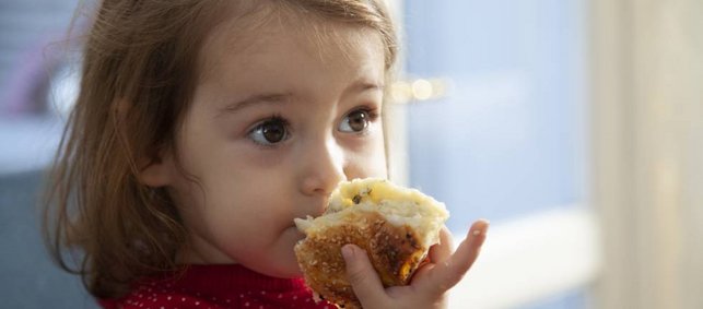 Ein etwa zweijähriges Mädchen isst ein weiches Stück Fladenbrot mit Sesam.
