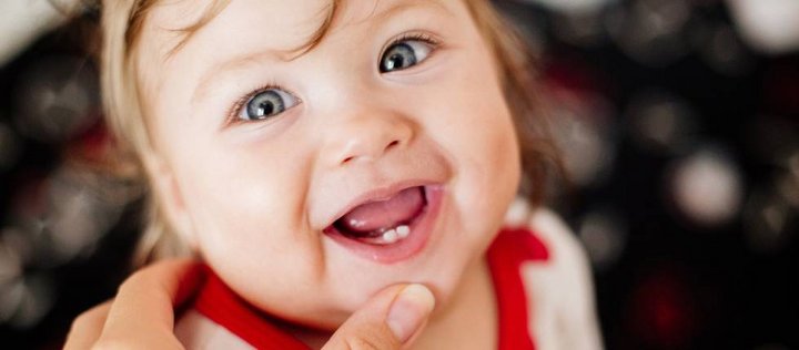 Baby lächelt in die Kamera, zwei erste Zähnchen sind in seinem Mund zu sehen.
