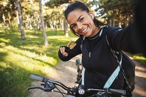 Lächelnde Frau mit Fahrrad auf Waldweg schaut in Kamera