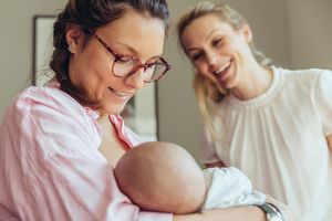 Hebamme lächelt mit Mutter, Baby