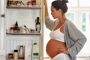 Schwangere schaut nachdenklich in Kühlschrank