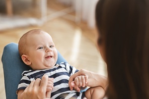 lächelndes Baby liegt auf Schoss einer Frau und schaut sie an