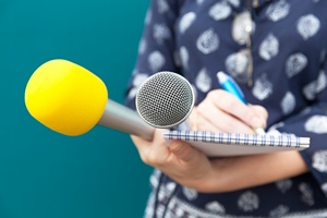 Eine Person hält zwei Mikrofone und einen Block mit Stift