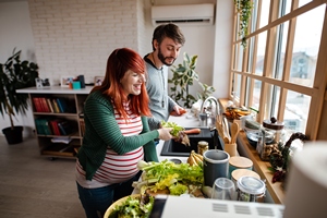 Ein schwangeres Paar steht gut gelaunt in der Küche und bereitet Gemüse zum Kochen vor.