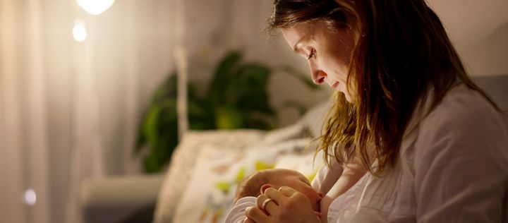 Frau stillt Neugeborenes abends im Schlafzimmer